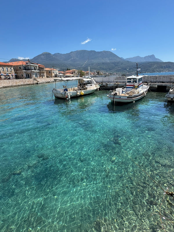 Barcas de pescadores en un puerto de agua cristalina, con casas de piedra y montañas