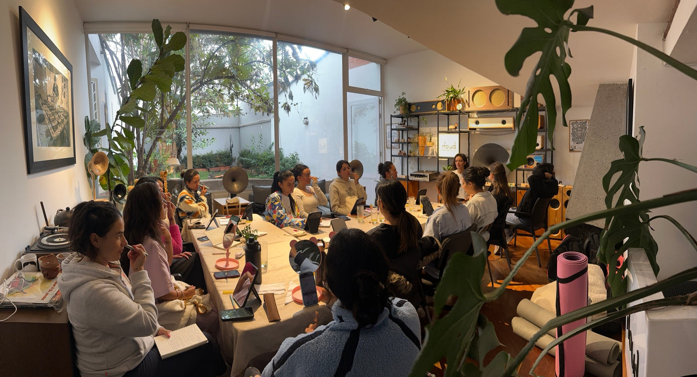 Una mesa larga junto a un ventanal con plantas: el grupo practica reflexología facial con la varita en el encuentro de Bogotá