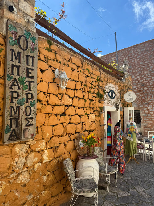 Muro de piedra dorada con letrero pintado a mano, flores y vestidos de colores