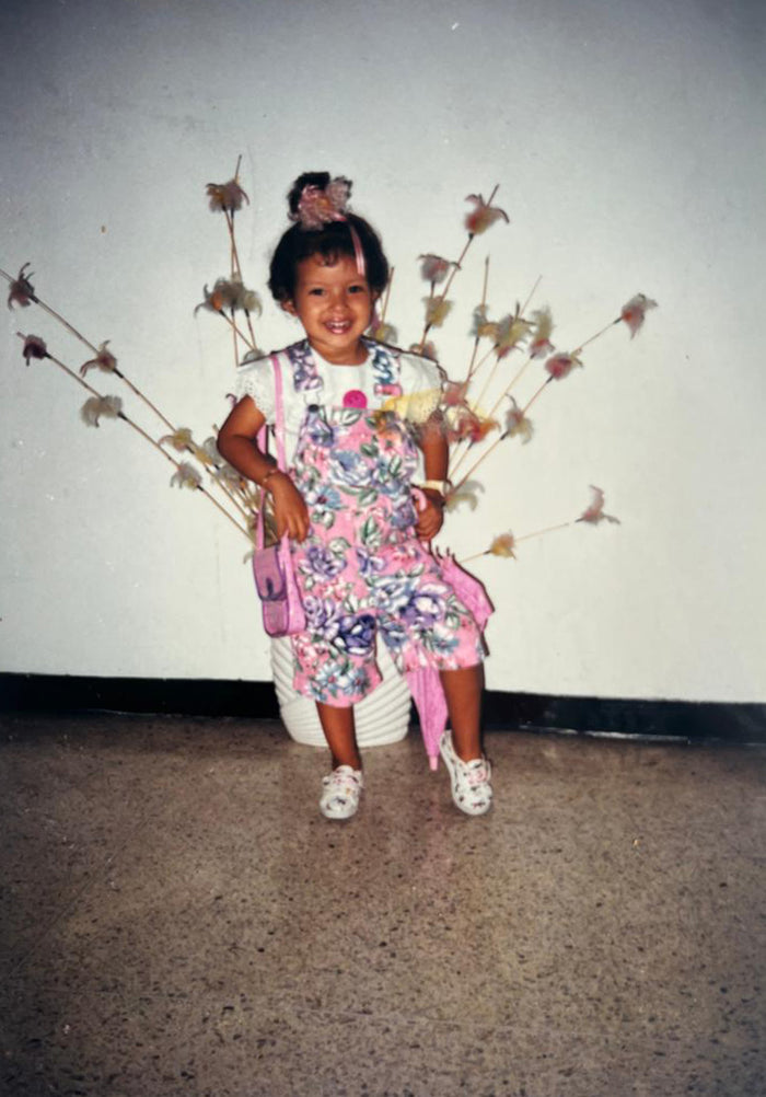 Gia de niña, sonriendo, con un enterizo de flores y un bolsito rosado