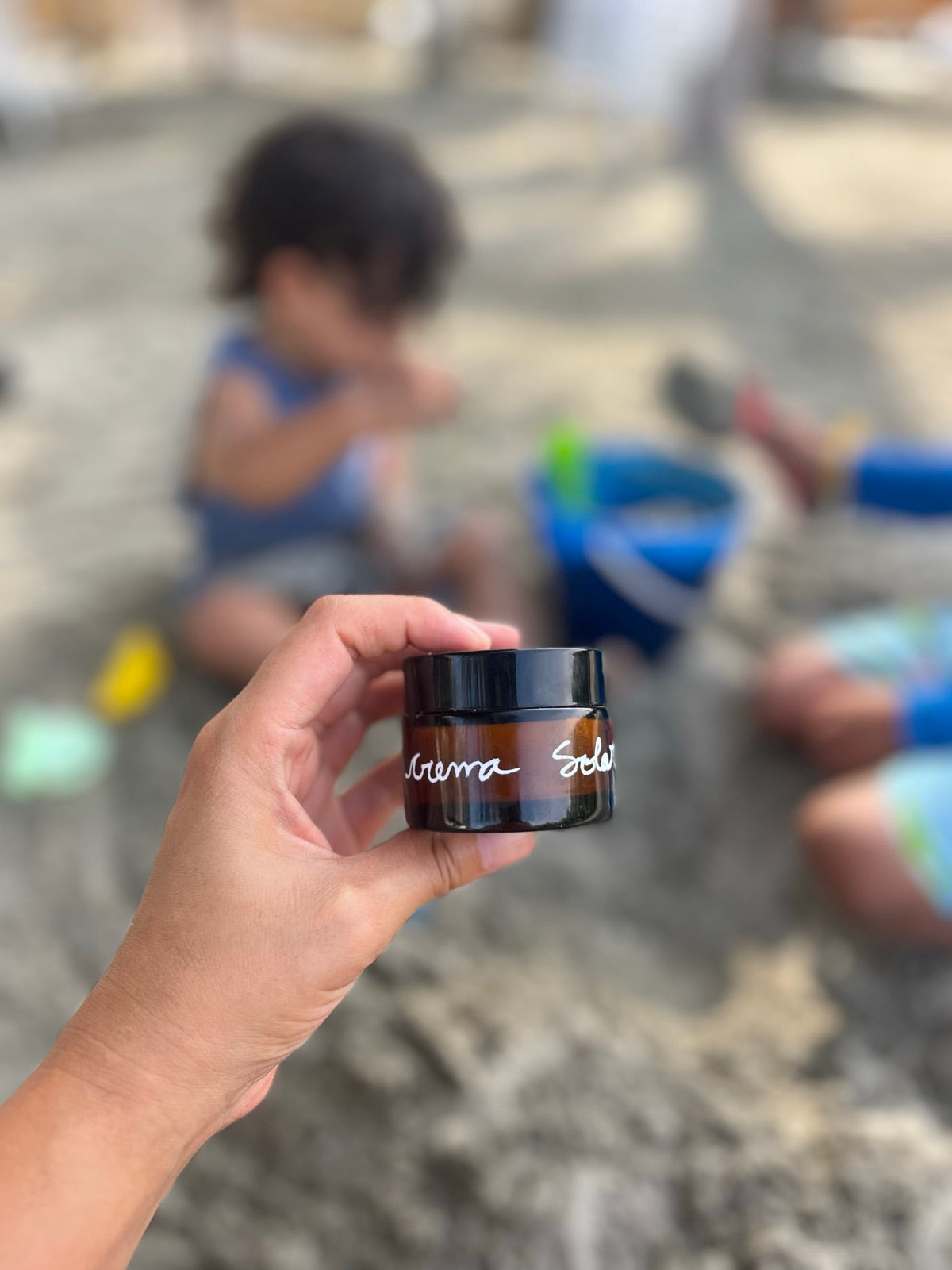 Crema solar con el nombre escrito a mano, en la playa, con los niños jugando en la arena al fondo